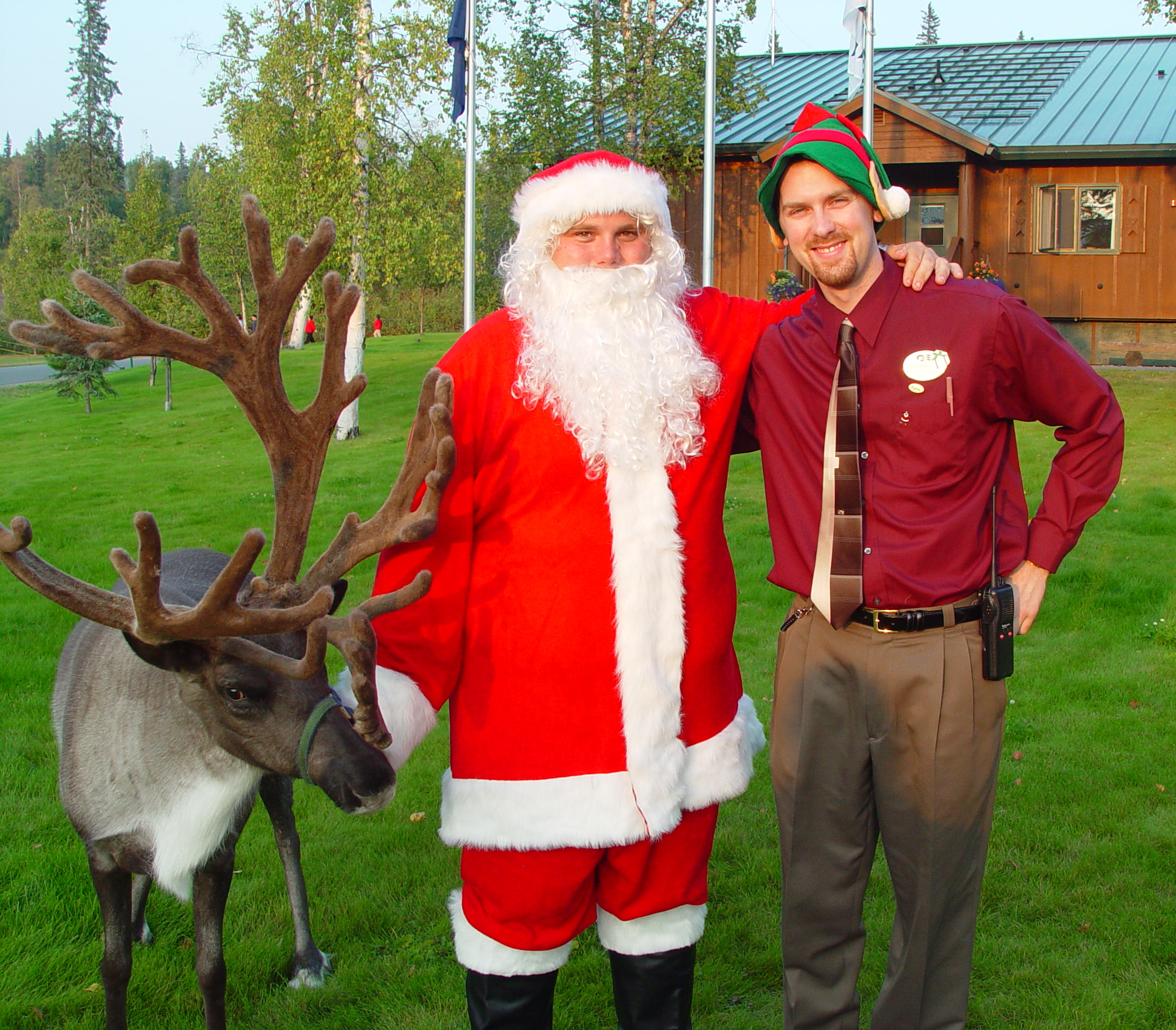 Lodge staff wearing an elf hat posing for a photo with Santa and a reindeer with large, velvety antlers.