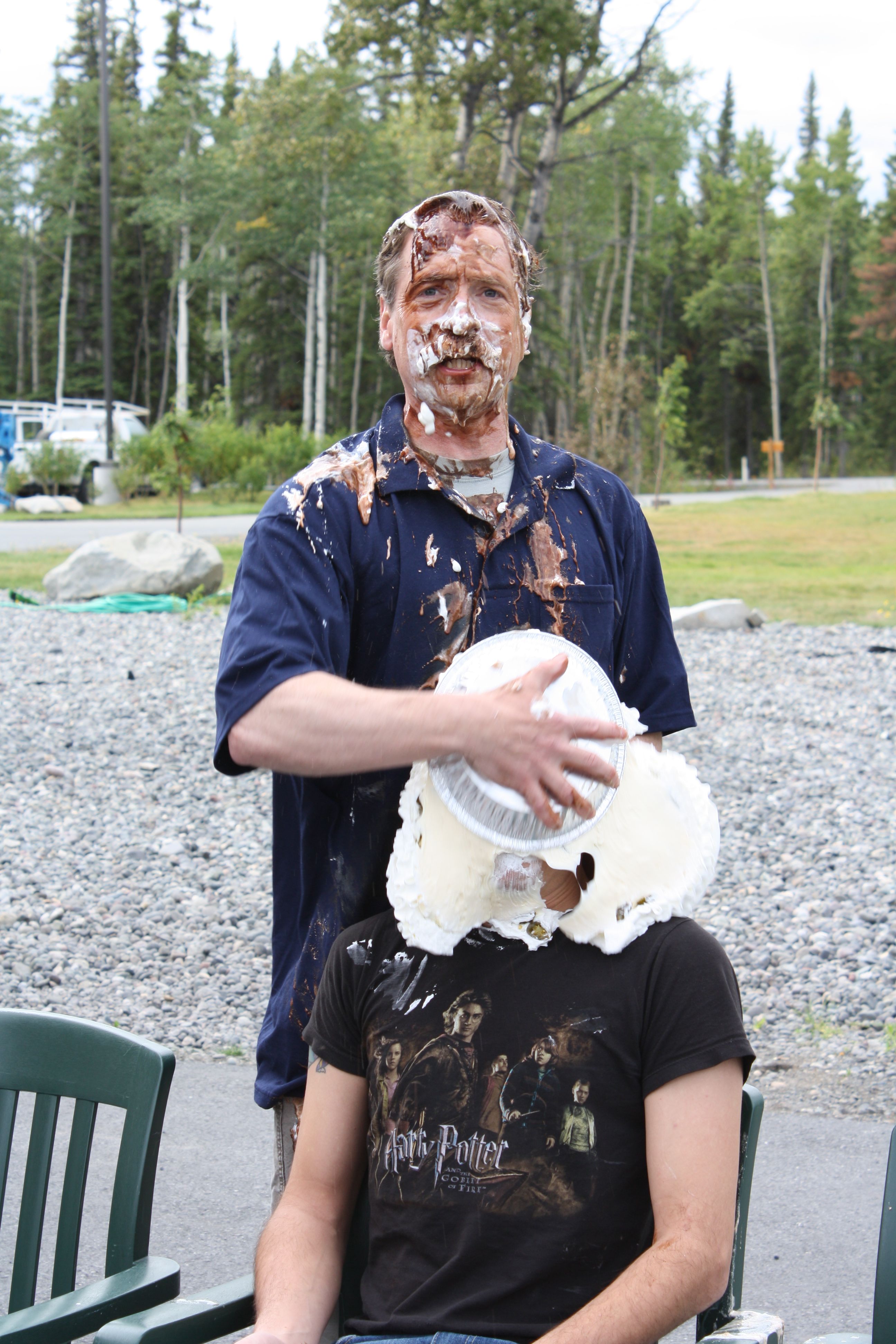 Man covered in whipped cream and chocolate smashing a pie in a man's face. pie in the face