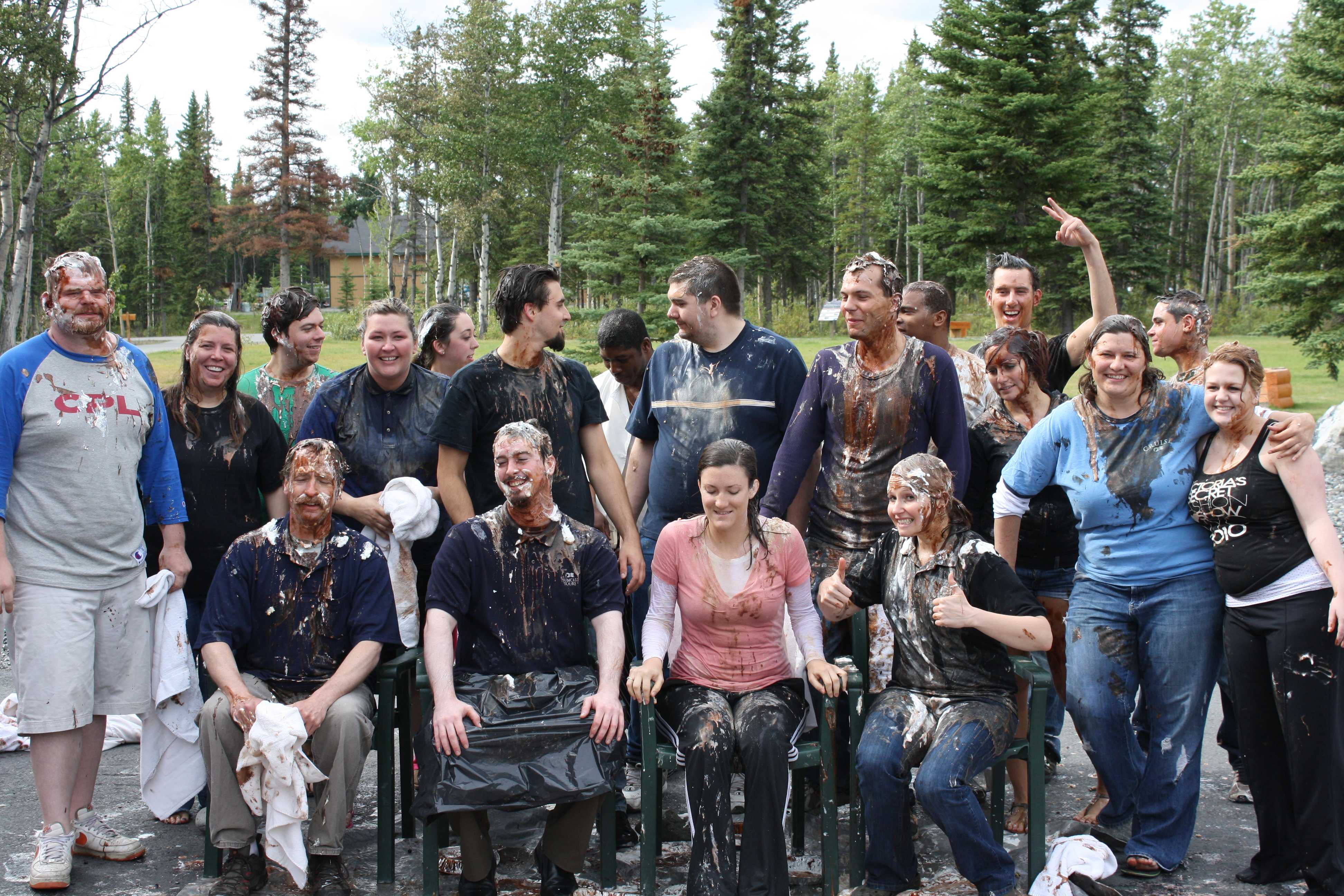 A group of over a dozen people covered in whipped cream in chocolate enjoying each other. Pie in the Face group photo