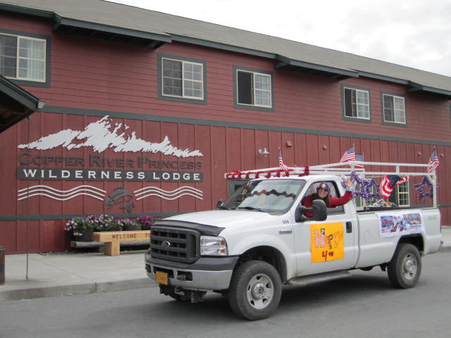 Copper River Princess Wilderness Lodge employee Rebecca Martz waves while participating in Glennallen's Fourth of July parade. Photo courtesy Princess Lodges. employee driving white truck decorated in red white and blue waves while participating in the Fourth of July parade.