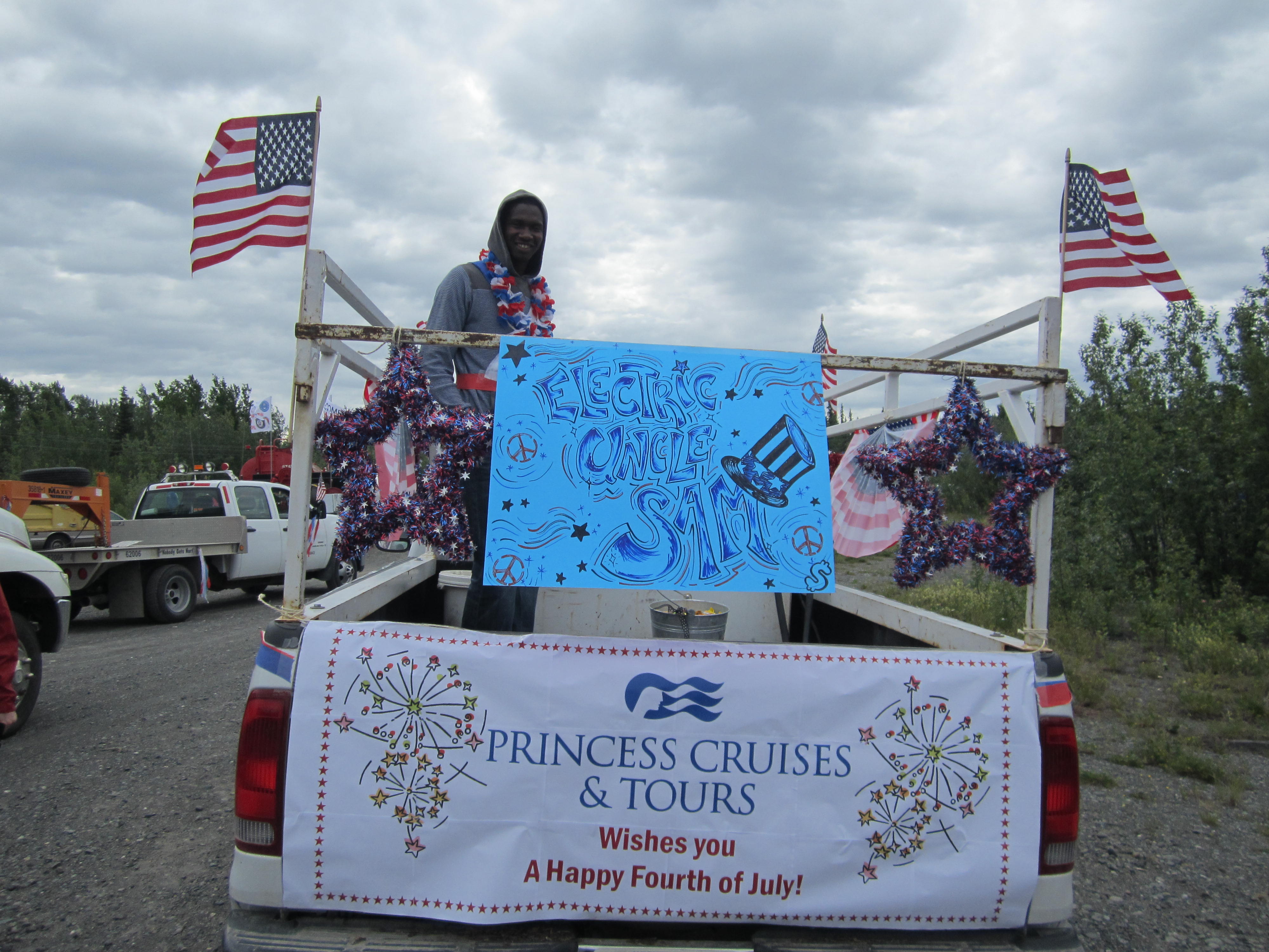 Copper River Princess Wilderness Lodge's June employee of the month, David Jonas, in Glennallen's Fourth of July parade. Photo courtesy Princess Lodges. photo of employee in the truck decorated with red white and blue and "Electric Uncle Sam" and Princess wishes you a happy Fourth of July" signs.